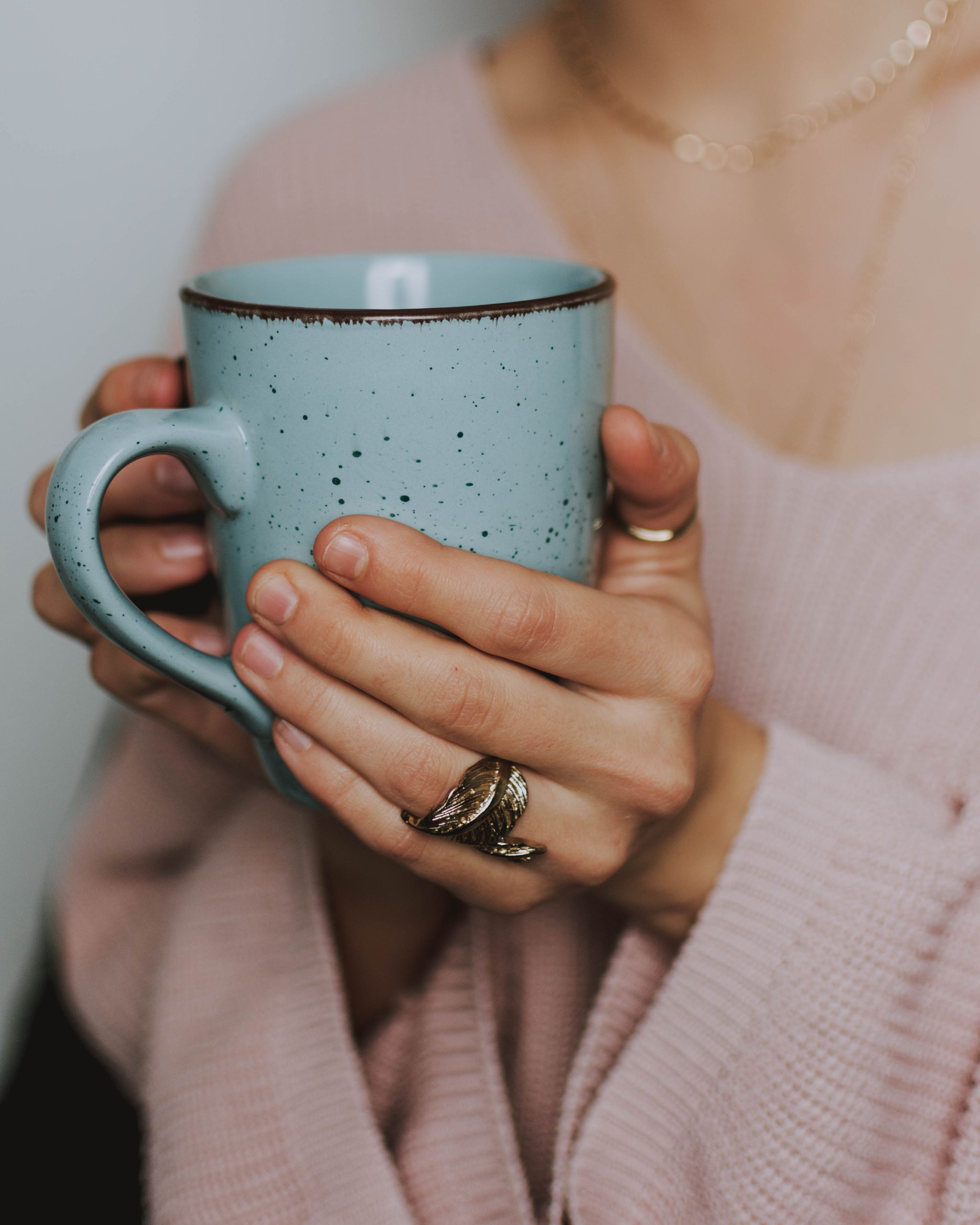 warm hand essentials with A close-up of a woman's hands holding a blue ceramic mug, wearing a cozy sweater.