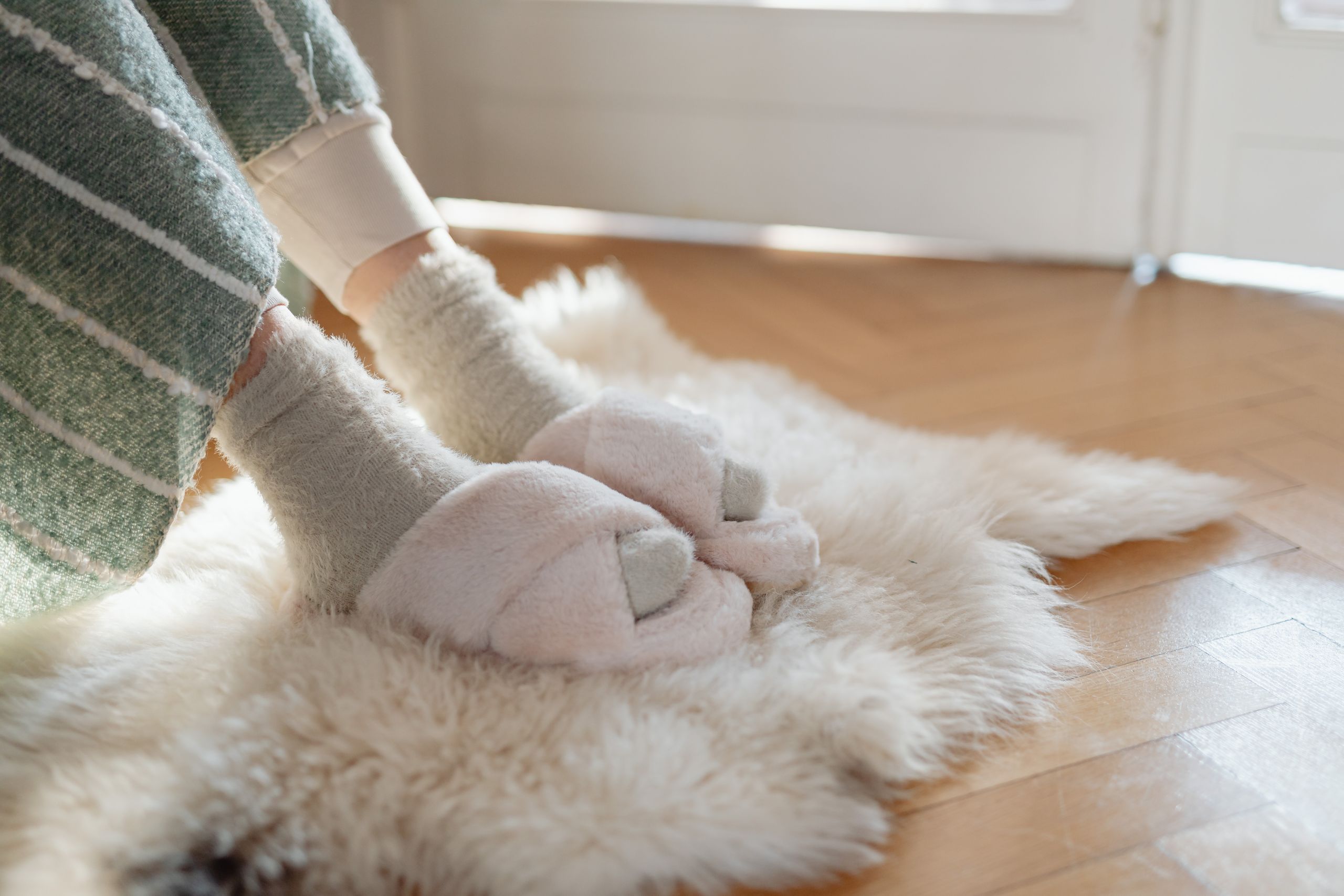 Warm slippers and socks on a fluffy rug by the sunlight, creating a cozy home atmosphere.
